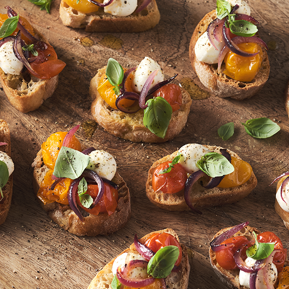 Small sandwiches topped with cherry tomatoes and mozzarella, decorated with basil leaves” data-udi=